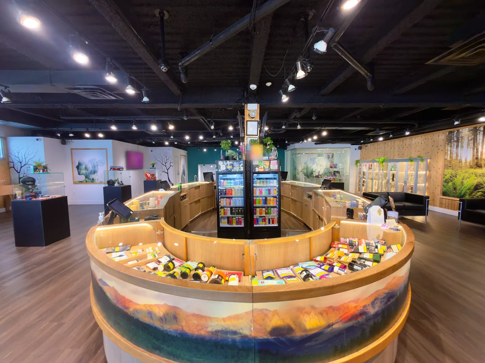 Inside WestCanna Broadway: the round wooden counter with its mountain wrap, the fridges, the display cabinets and the forest mural wall.