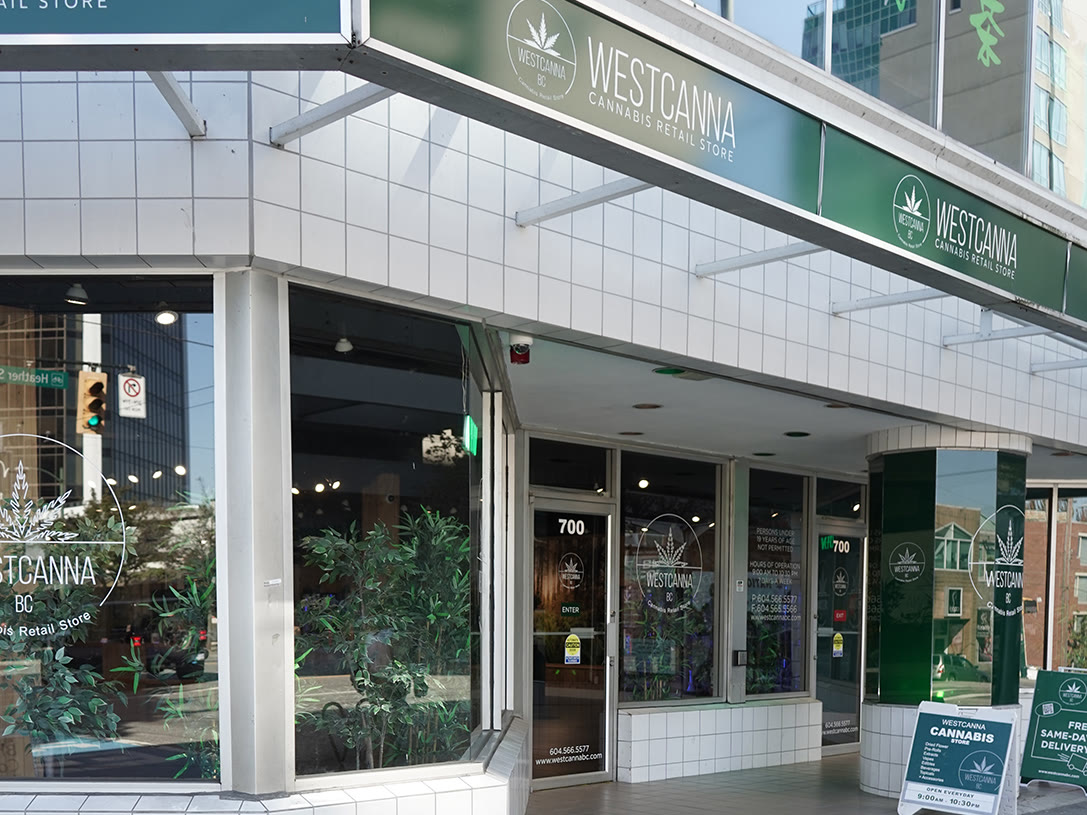 The WestCanna BC store at 700 West Broadway: white tile, a deep-green fascia with the WESTCANNA sign, plants in the window. No person is in frame.